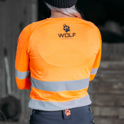 Photo of woman standing in work shed, wearing high visibility orange workshirt.