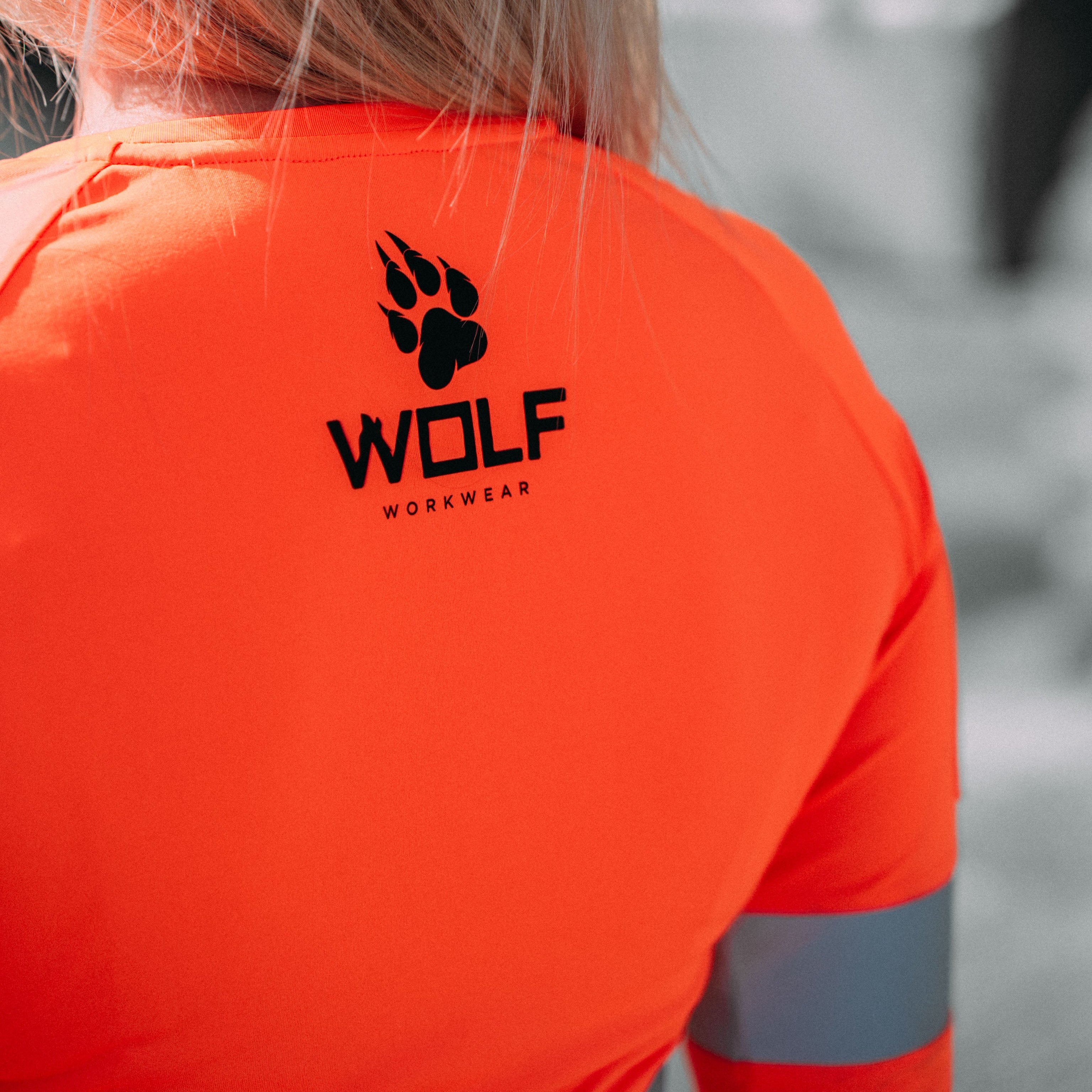 Up Close photo showcasing the detail on the back of an orange long sleeve high visibility Wolf Workwear shirt, with the logo.
