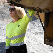 Woman standing on mining site, wearing yellow high visibility long sleeve shirt.