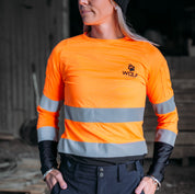 Woman standing in work shed wearing an orange high  visibility work shirt.