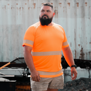 A man wearing an orange high-visibility T-shirt with reflective stripes, standing in front of a blue background with a rugged metal structure.