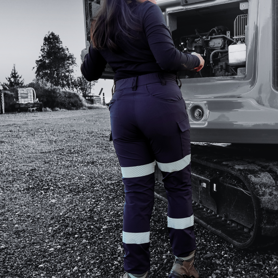 Person wearing navy work pants with reflective stripes standing next to a large vehicle.