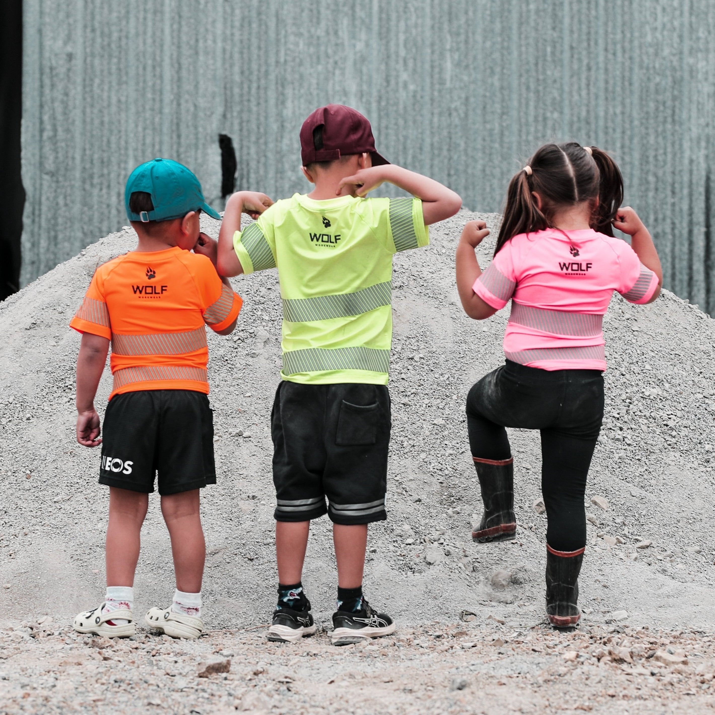 Three kids standing in industrial yard facing the other way, with high visibility Wolf t-shirts on
