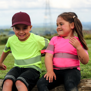 Two kids sitting at a playground wearing yellow and pink t-shirts and laughing
