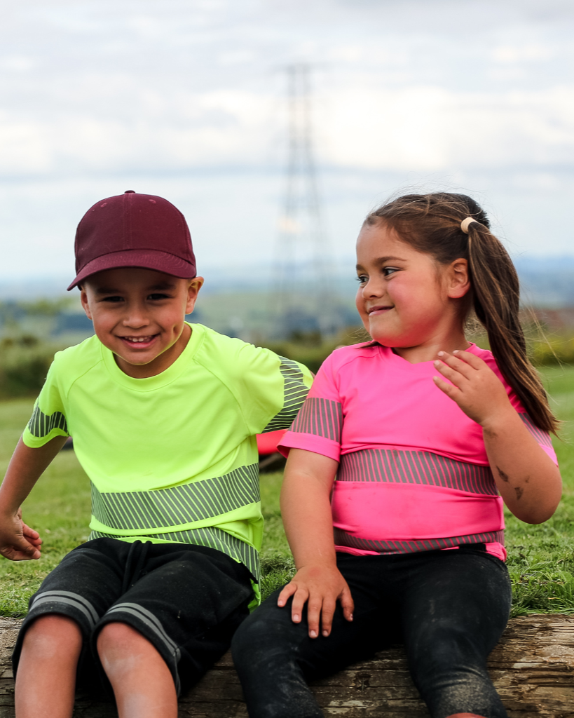 Two kids sitting at a playground wearing yellow and pink t-shirts and laughing