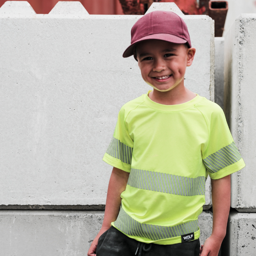 Boy standing in industrial yard wearing yellow high visibility t-shirt