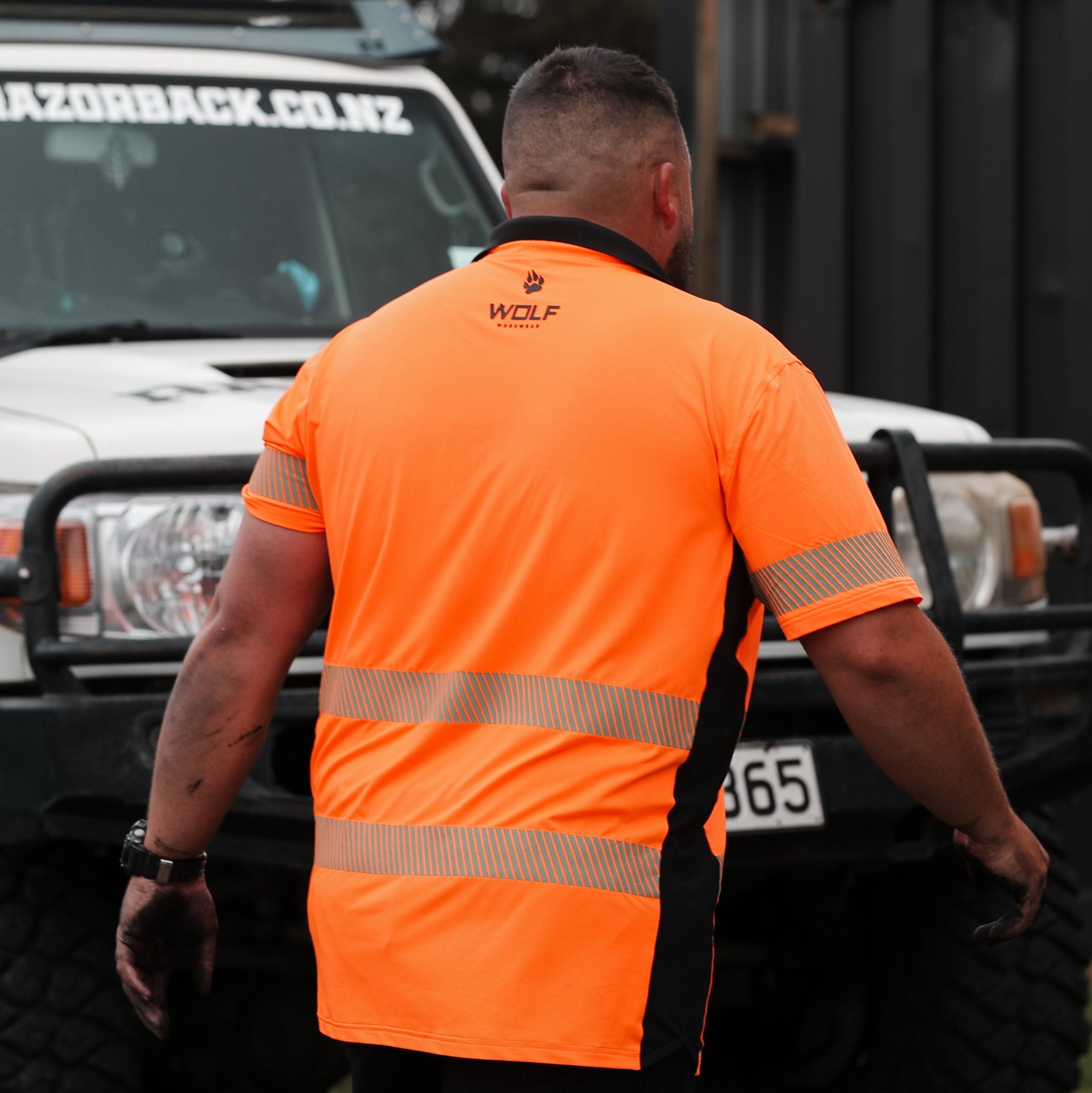 Man walking away with orange high visibility t-shirt on, WOLF workwear logo on the back of it.