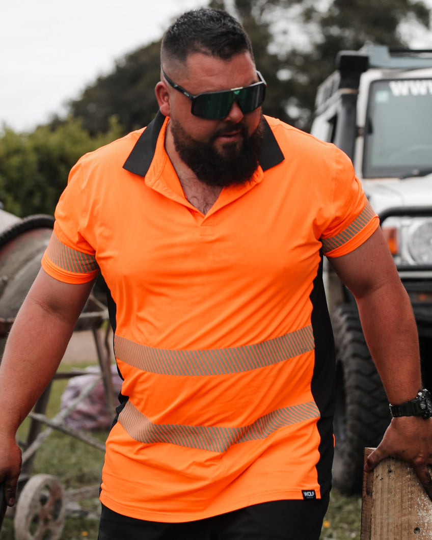 Man walking on work site wearing orange high visibility t-shirt and sun glasses with four wheel drive car and concrete mixer in the background