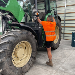 Person in orange safety vest working on a green tractor in a garage.