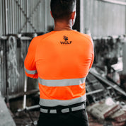 Man standing with back to the camera wearing long sleeve orange high visibility work shirt.