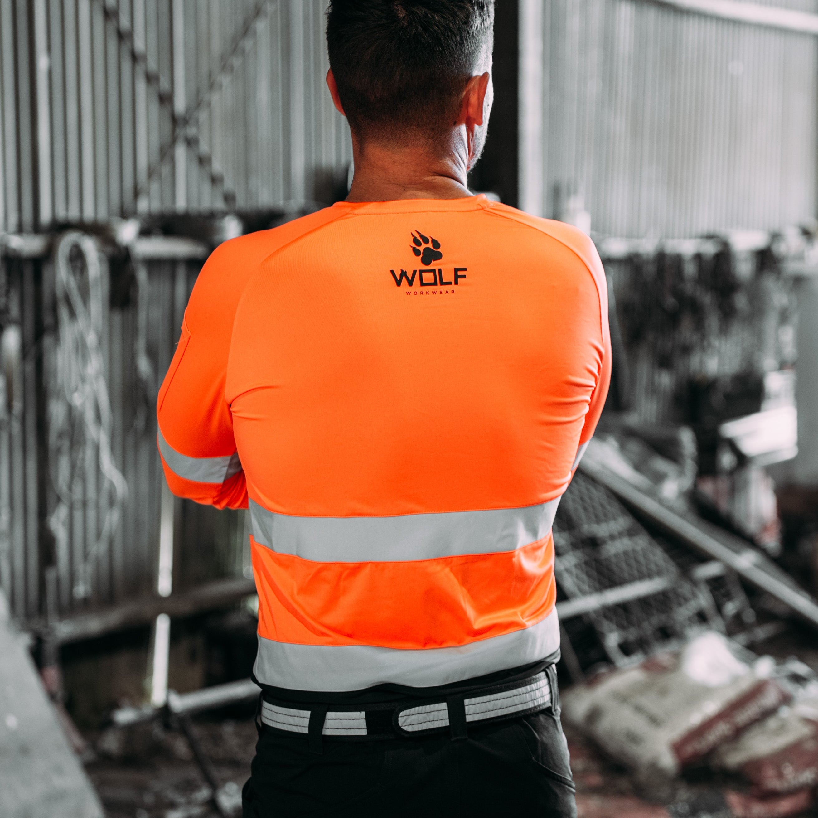 Man standing with back to the camera wearing long sleeve orange high visibility work shirt.