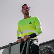 Man standing outside on a work site wearing sunglasses and high visibility long sleeve yellow shirt.
