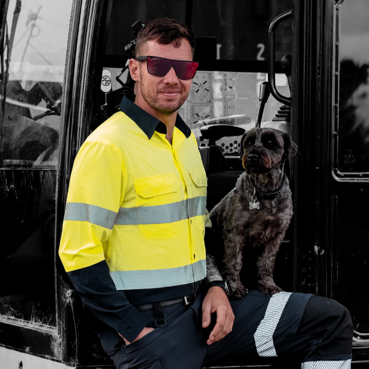 Person in high-visibility workwear with a dog sitting on a  digger