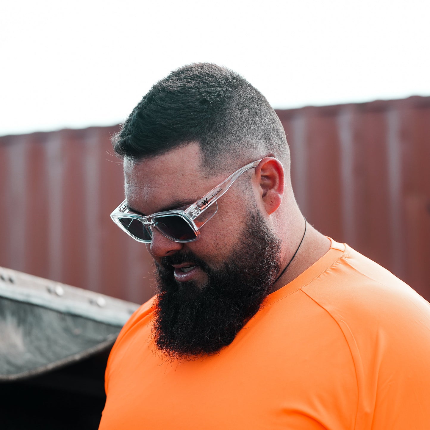 Tradie wearing Wolf Workwear SpecOps self-tinting safety glasses outside in an industrial yard, wearing high visibility t-shirt.