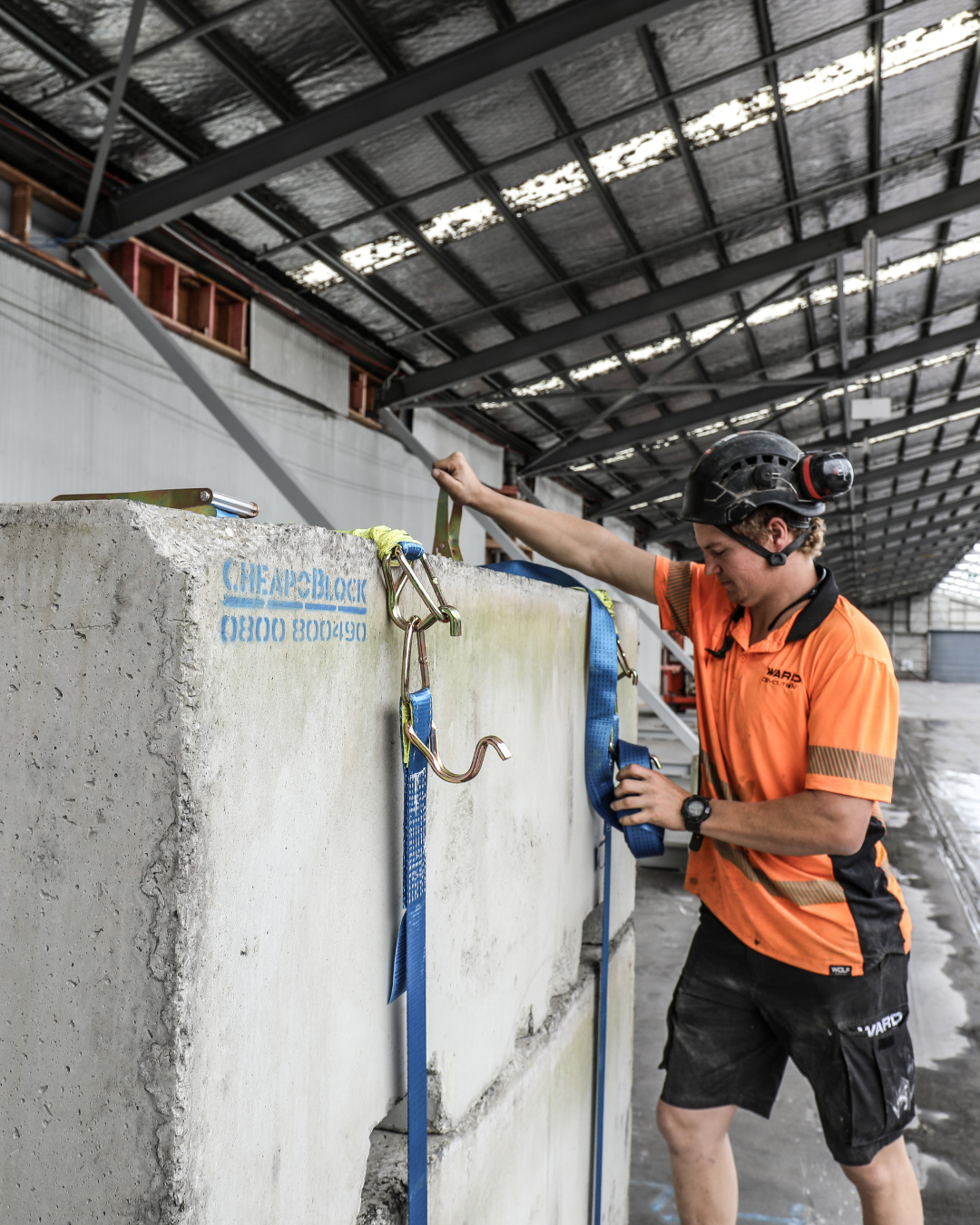 Person in an orange shirt and black helmet working with concrete blocks in a warehouse.